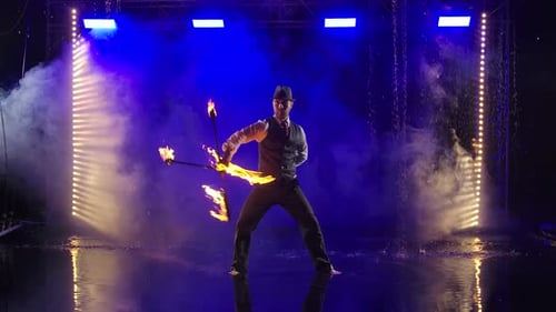 Man Juggling Fire Stick Under Blue Stage Lights