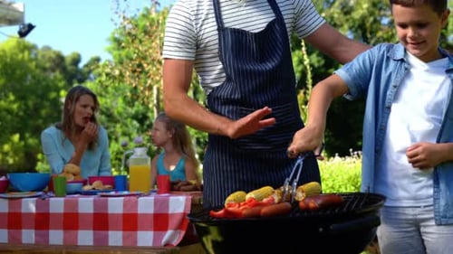 Father and son grilling sausages and corns on barbecue
