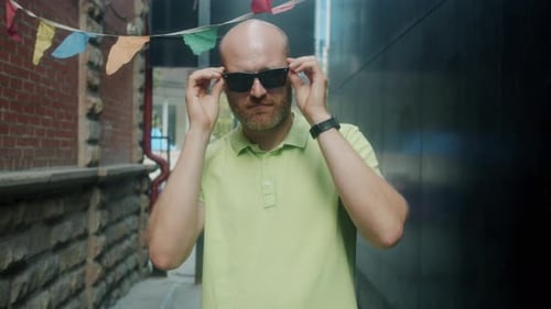 Slow Motion Portrait of Attractive Guy Touching Sun Glasses Looking at Camera Outside in City Street