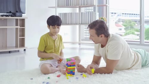Dad and son playing jigsaw puzzle game toy, building colorful blocks tower together