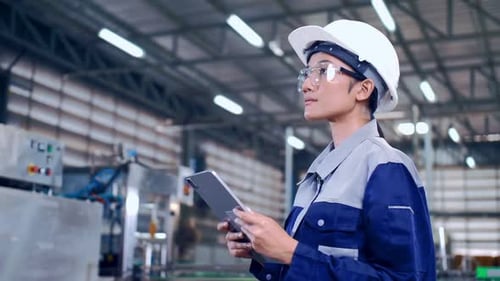 Engineer is using a tablet to check the machine's control system in a factory.