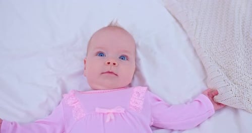 Portrait, a Baby with Big Blue Eyes Lies on a Light Bed. Beautiful Baby Smiles and Moves His Arms