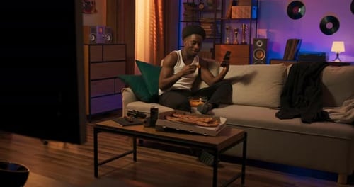 Handsome Muscular Man Sitting on a Couch Wearing a White Tshirt Holding a Phone Sending Messages