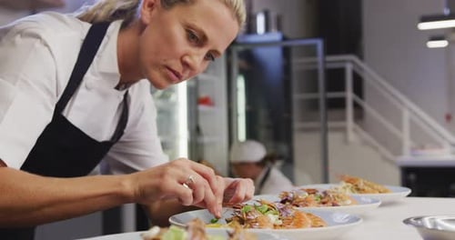 Caucasian female chef wearing chefs whites in a restaurant kitchen,putting food on a plate