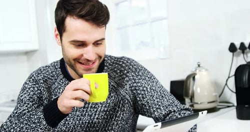 Man Drinking Coffee and Using Tablet in Kitchen
