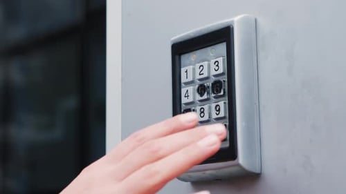 Female fingers entering password at electronic door entry lock.
