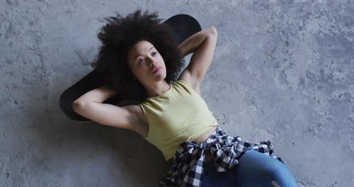 Mixed race woman in an empty building lying on a skateboard