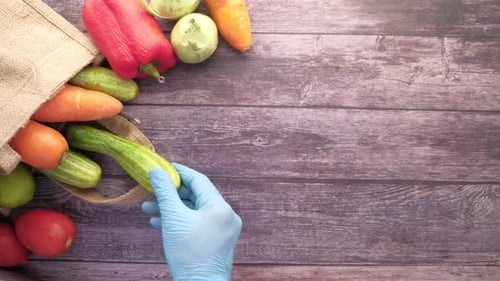 Guantes manos en mano para sacar verduras de una bolsa reutilizable: vista superior de verduras