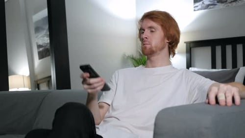 Man Watches TV on Couch at Home with Remote