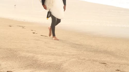 Ein junger Mann hält sein Surfbrett am Strand.