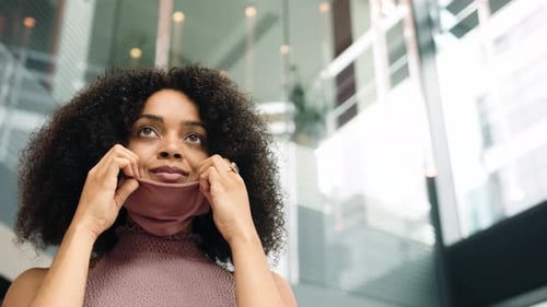 Businesswoman Putting On Face Mask In Modern Open Plan Office During Covid-19 Pandemic