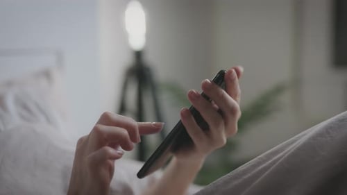 Unrecognizable Woman Uses Smartphone While Lying in Bedroom