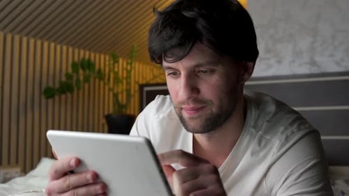 Man Uses Tablet While Lying in Bed