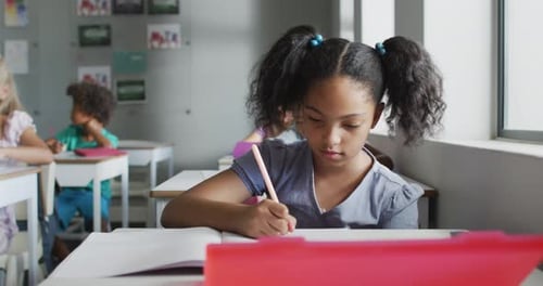 Elementary School Student Writes at Desk in Classroom