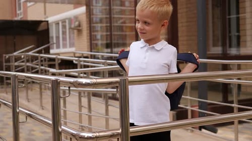 Portrait of a Little Boy Who Puts on a Backpack in the School Yard