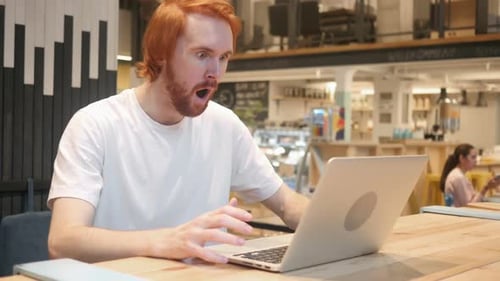 Man Using Laptop Reacts with Surprise in Cafe
