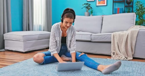 Woman Using Laptop and Headphones on Floor