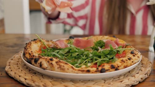 Chef in the Pizzeria Prepares a Pizza and Decorates It with Prosciutto. Green Herbs Close Up