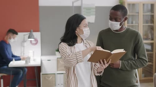Woman Explains Notebook to Man in Mask at Office