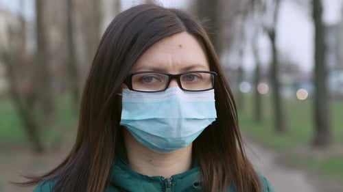 A Young Girl in Glasses and Medical Mask Stands on the Street