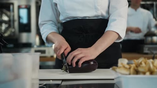 Close-up: The chef cuts an eggplant, preparing a delicious dish in a restaurant.