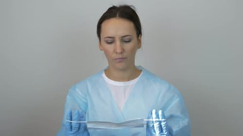 Femme en uniforme de médecin et gants bleus chirurgicaux portant un masque de protection se préparant à la chirurgie
