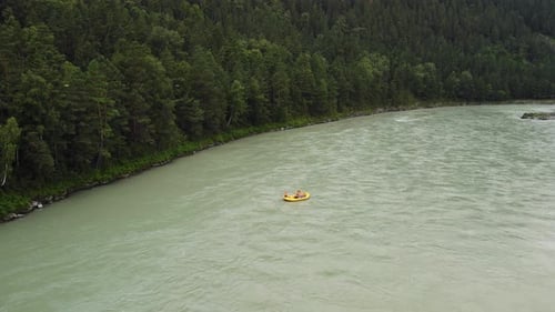 A Group of People in Orange Vests Yellow Helmets and Boats Raft Down the River Along the Hilly