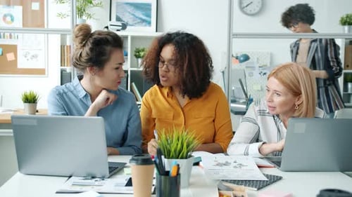 Multiracial Female Team Sharing Ideas Talking and Using Computers Working in Office Together