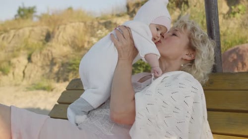 Woman Holding Infant Up in the Air on Bench