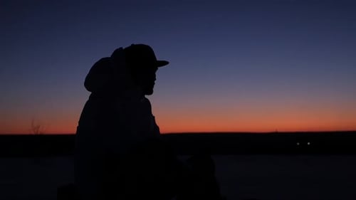 Ein junger Mann in einer Mütze sitzt nachdenklich bei Sonnenuntergang und träumt