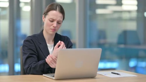 Woman Typing at Desk Rubs Wrist in Office