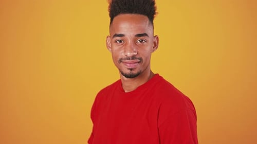 Young African American Guy Turning to Camera and Smiling Orange Background