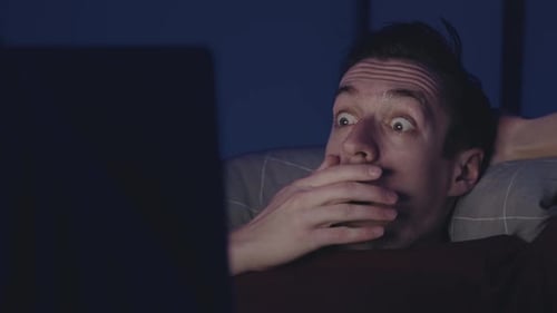 Man Watching Screen with Shocked Expression at Night
