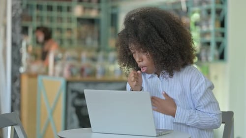 Sick African Woman with Laptop Coughing in Cafe