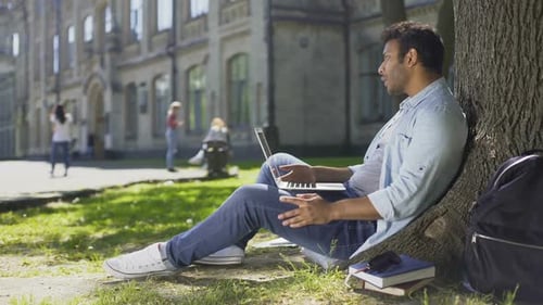 Mixed-Race Young Guy Using Laptop Under Tree, Getting Bad News, Disappointment