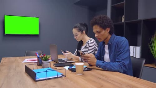 Two Workmates Use Phones in Office