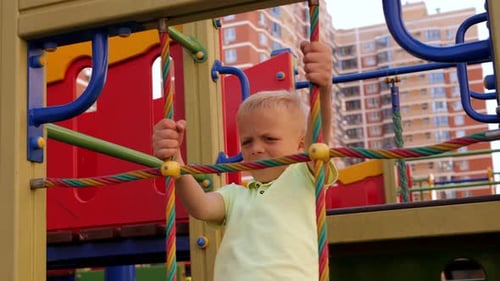 A Child Climbs a Grid in a Park on a Playground on a Hot Summer Day