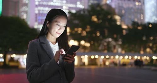 Woman Using Phone in Urban Park at Night