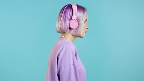 Hübsches Mädchen mit gefärbten violetten Haaren, Musik hören, lächeln, im Studio im Kopfhörer tanzen