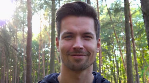 A Young Handsome Backpacker Smiles at the Camera in a Forest on a Sunny Day - Face Closeup
