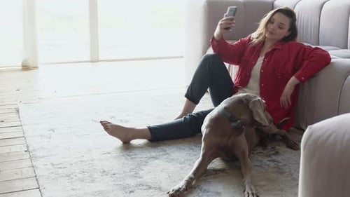 Woman with Dog Relaxing at Home with Smartphone