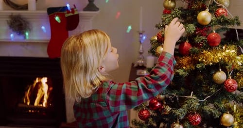 Child Decorating Christmas Tree by Fireplace at Home