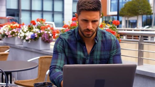 Man Works on Laptop at Outdoor Cafe