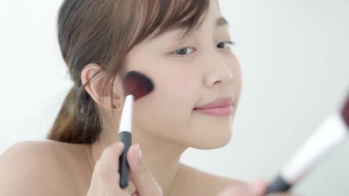 Beauty young asian woman smile with face looking mirror applying makeup with brush of cheek.