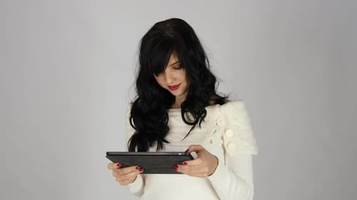 Portrait of a Laughing Woman Using Tablet Computer Isolated on a Gray Background, Looking at Camera