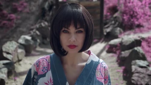 Brünette kaukasische Frau, gekleidet wie japanische Geisha, schaut in die Kamera und steht draußen auf Sakura