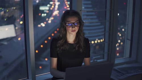 Girl Works in Office in Late Evening Against Background of Lights of the Night of the City. Young