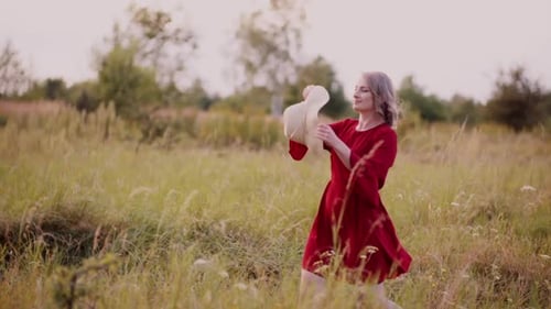 Woman in Red Dress Puts on Hat in Field