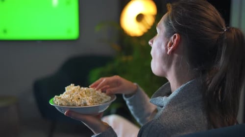 Woman Sitting on a Sofa in the Living Room in the Evening and Watching a Green TV Screen Mockup