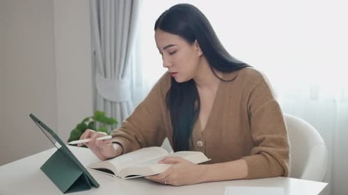 A woman creator is taking notes in a notebook working in front of her house about a book.